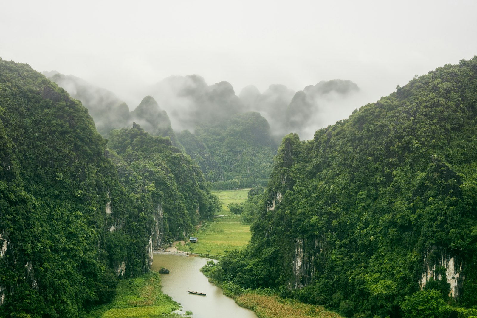 Misty karst mountains and a lush green river valley with a lone sampan in Ninh Binh, Vietnam